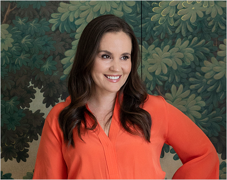 Woman in an orange shirt standing against a green leafy background