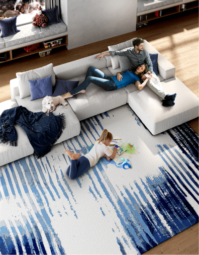 Family sitting in the living room on a couch and girl laying on a large blue and white designer rug.