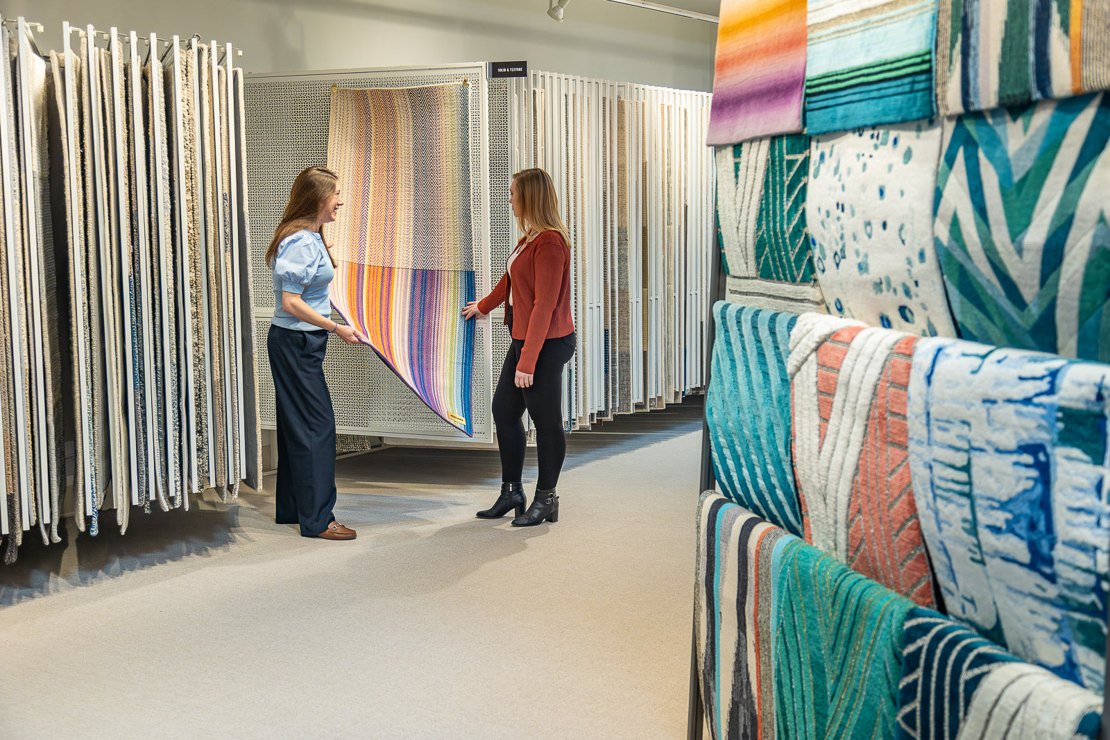 Two women in a STARK rug and carpet store examining colorful fabric samples