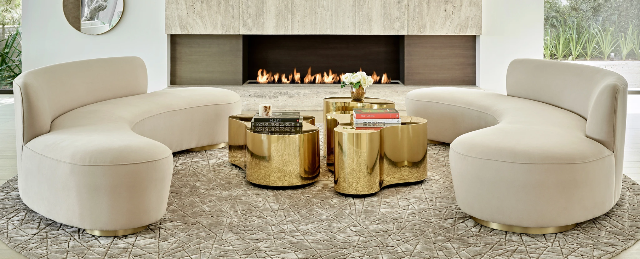 Modern living room with two rounded couches, fireplace, large designer rug and golden coffee tables.