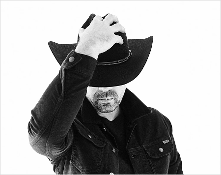 Man wearing a black cowboy hat and jacket on a white background