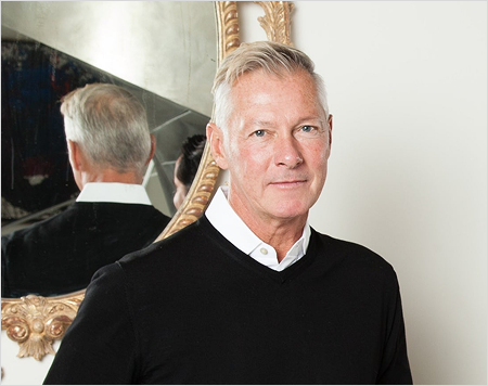 Man in a black sweater standing in front of a mirror with decorative frame.